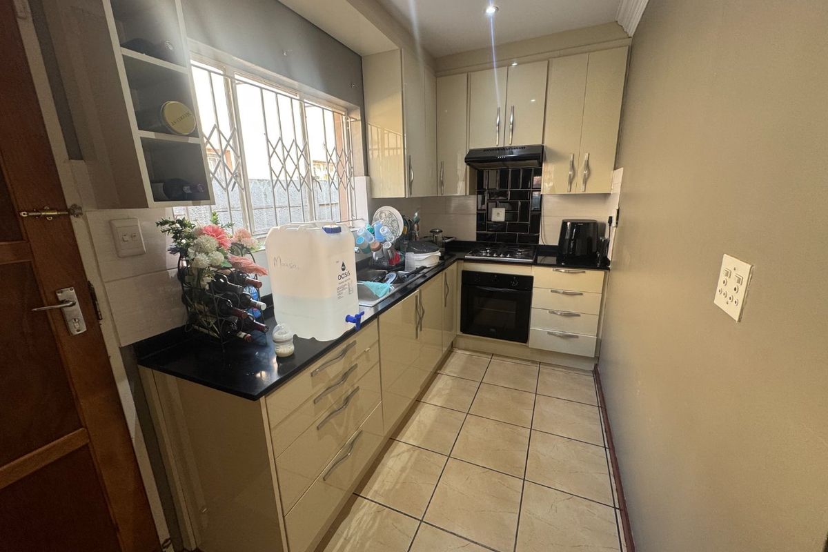 Compact kitchen featuring high-gloss cabinetry, granite countertops, built-in oven, gas hob, and tiled flooring with a security-fitted window.