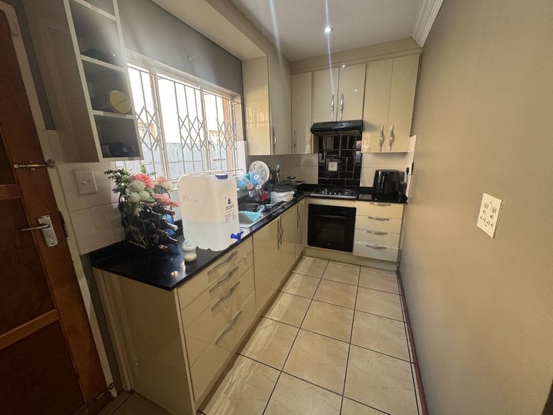 Compact kitchen featuring high-gloss cabinetry, granite countertops, built-in oven, gas hob, and tiled flooring with a security-fitted window.