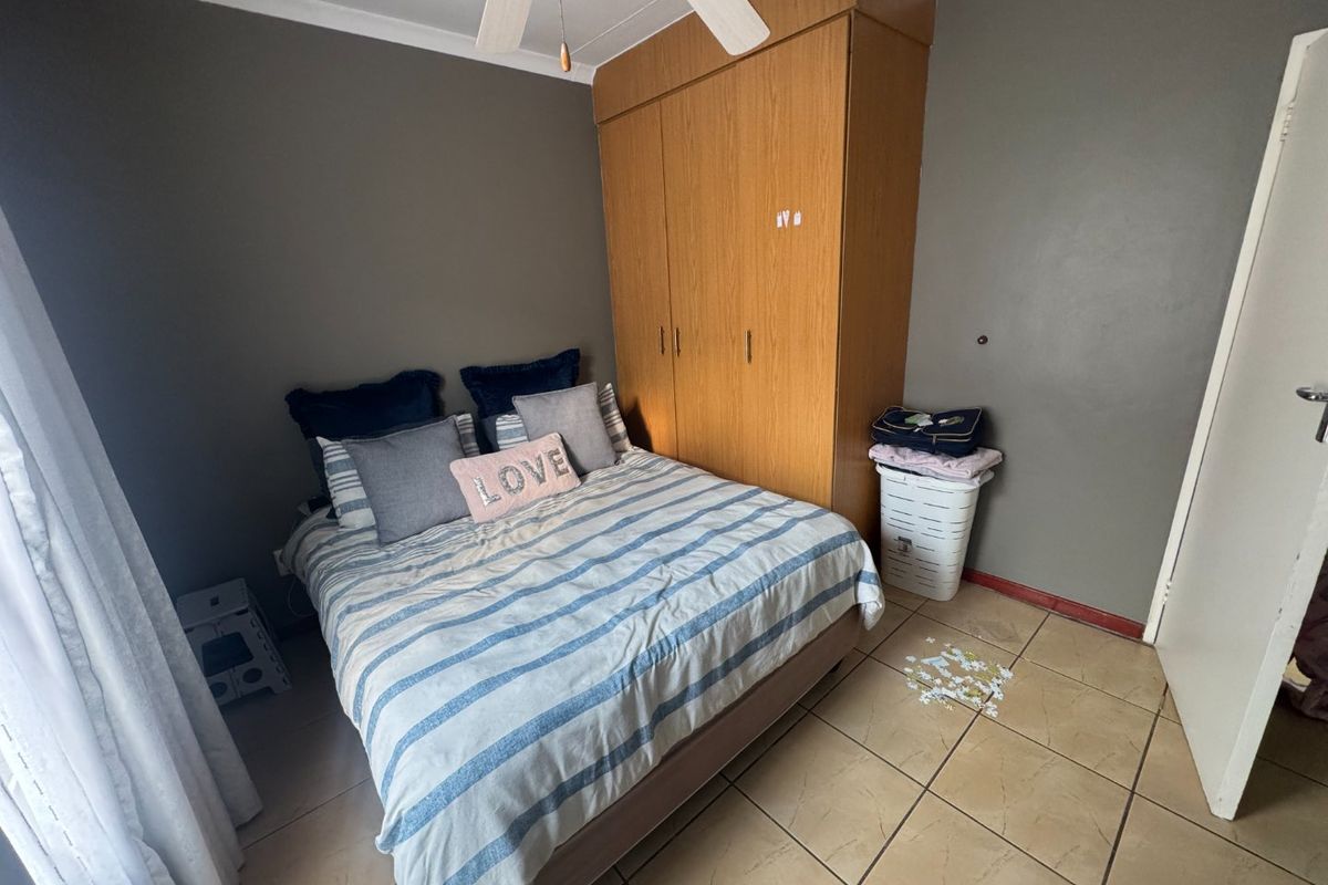 A functional bedroom featuring built-in wooden cupboards, a ceiling fan, and tiled flooring, offering a neutral base for potential updates.
