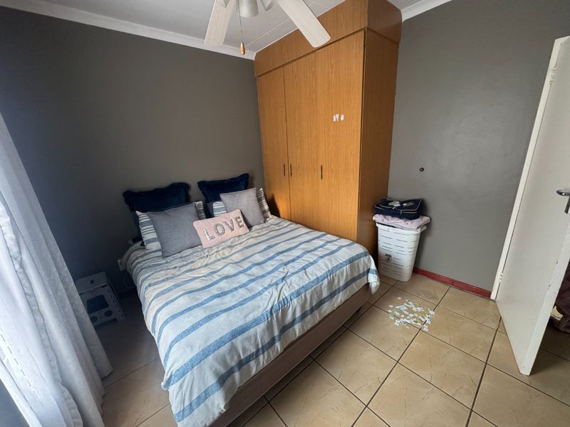 A functional bedroom featuring built-in wooden cupboards, a ceiling fan, and tiled flooring, offering a neutral base for potential updates.