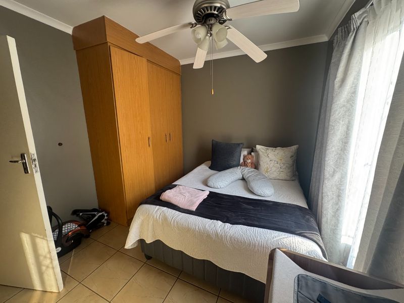 A compact bedroom featuring tiled flooring, a built-in wooden wardrobe, and a ceiling fan, providing a functional and comfortable living space.
