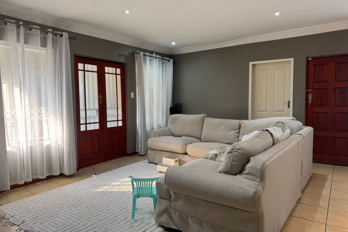 A spacious living room featuring tiled flooring, recessed downlights, decorative cornicing, and timber-framed glass doors providing natural light.