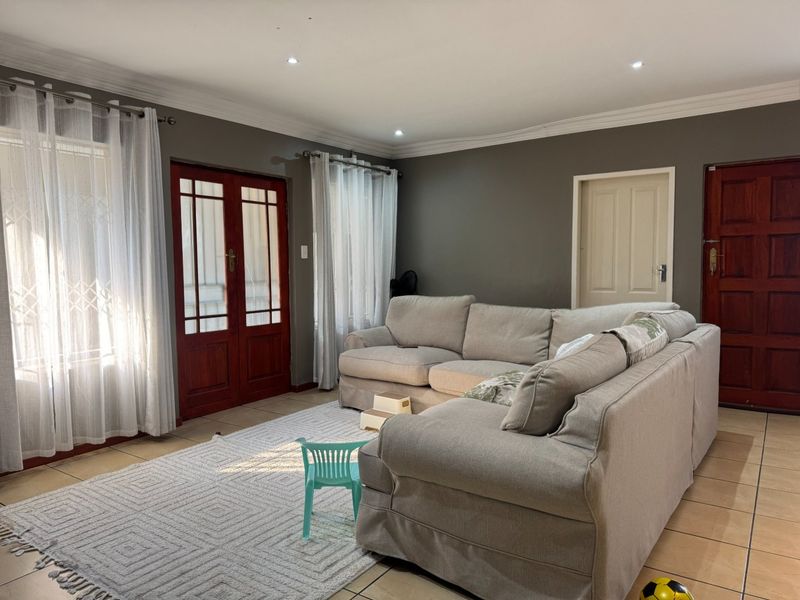 A spacious living room featuring tiled flooring, recessed downlights, decorative cornicing, and timber-framed glass doors providing natural light.