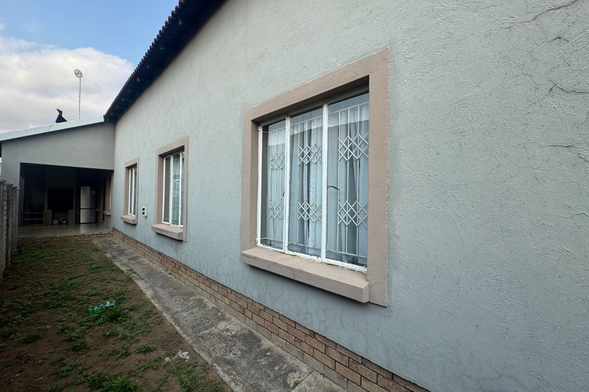 Rear exterior view of the townhouse featuring a plastered facade, brick plinth, and security-fitted windows along the side path.