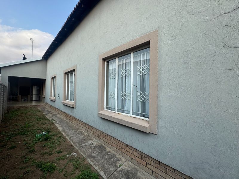 Rear exterior view of the townhouse featuring a plastered facade, brick plinth, and security-fitted windows along the side path.