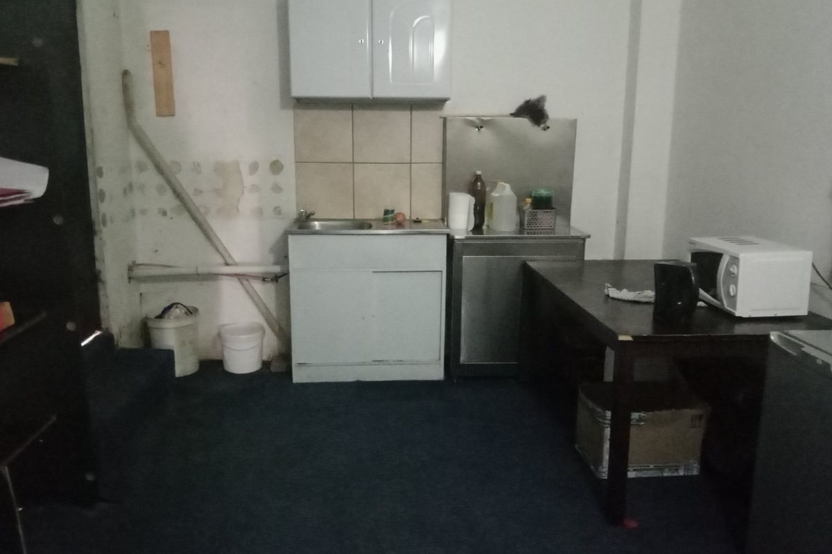 A basic kitchenette area featuring a sink, wall-mounted cabinets, and a stainless steel prep station, requiring cosmetic updates and wall repairs.