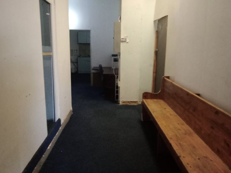 A commercial hallway featuring dark carpet flooring and an exposed electrical distribution board, leading towards an adjacent office or utility space.