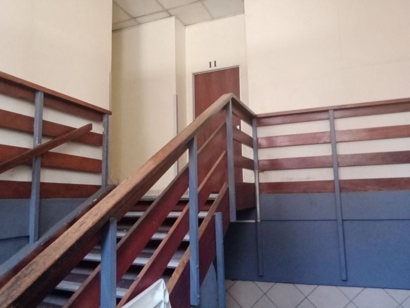 Commercial hallway featuring a staircase with wooden handrails, metal balustrades, and tiled flooring leading to office unit 11.