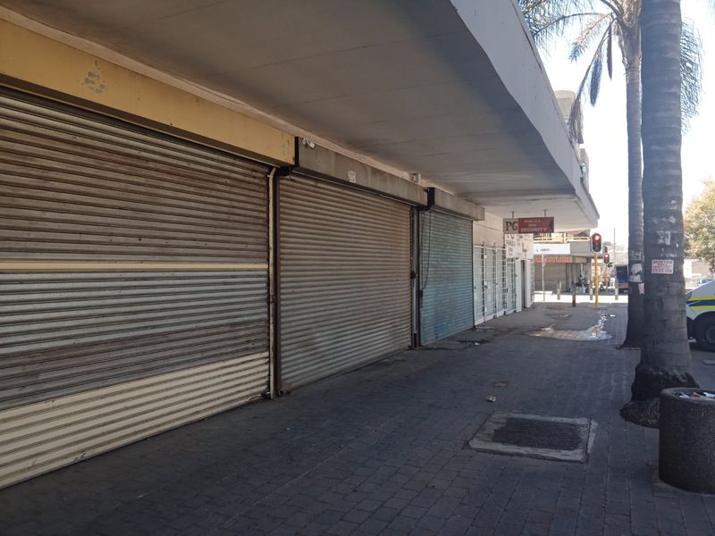 Commercial storefront exterior featuring multiple roller shutter doors, a concrete canopy, and a paved sidewalk area.