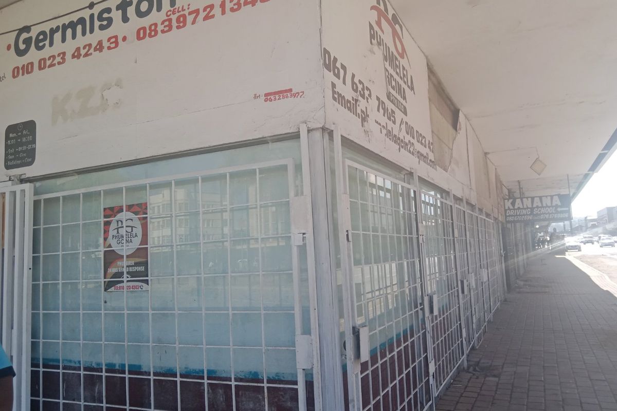 Commercial street-level shopfront featuring security gates and signage, located along a paved pedestrian walkway.