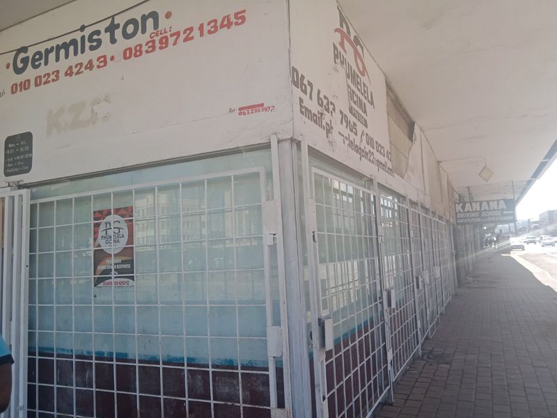 Commercial street-level shopfront featuring security gates and signage, located along a paved pedestrian walkway.