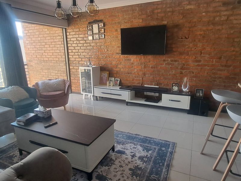 Open-plan living area featuring an exposed brick wall, tiled flooring, and direct access to a balcony through large sliding glass doors.