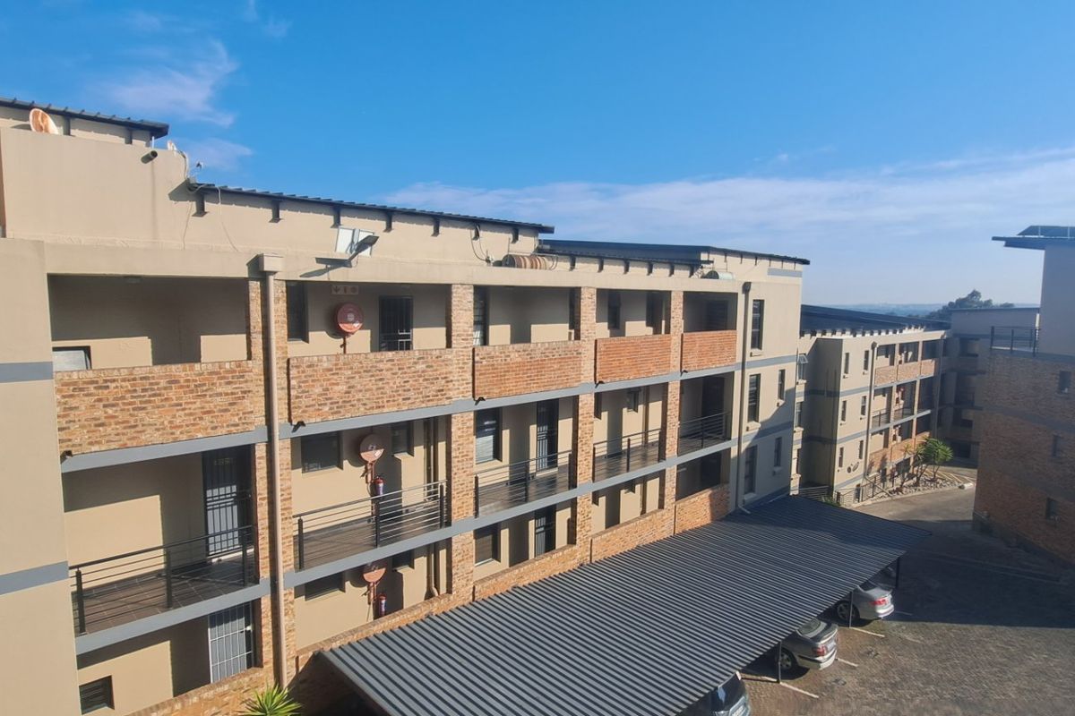 An elevated view of a multi-story townhouse complex featuring brick and plaster facades, private balconies, and covered parking bays.