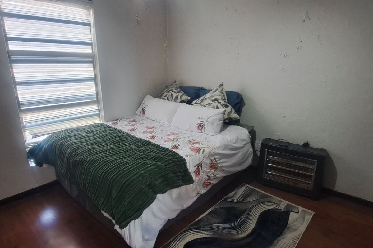 A bedroom featuring laminate flooring and zebra blinds, currently showing signs of wall surface deterioration requiring maintenance and cosmetic repair.