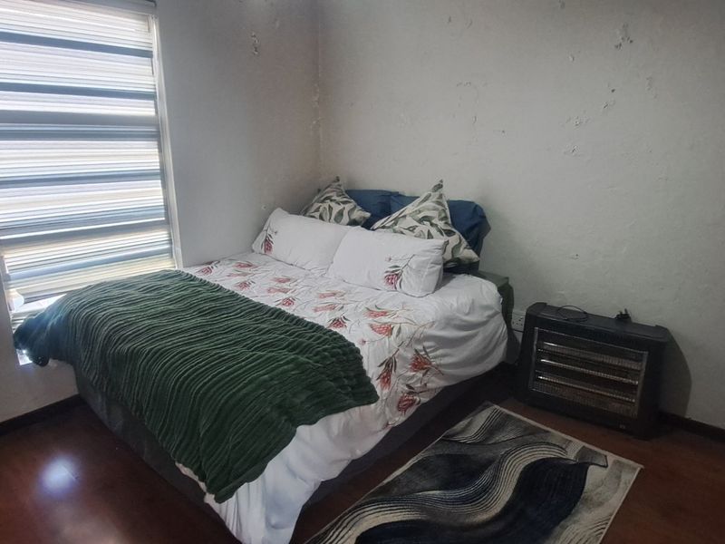 A bedroom featuring laminate flooring and zebra blinds, currently showing signs of wall surface deterioration requiring maintenance and cosmetic repair.