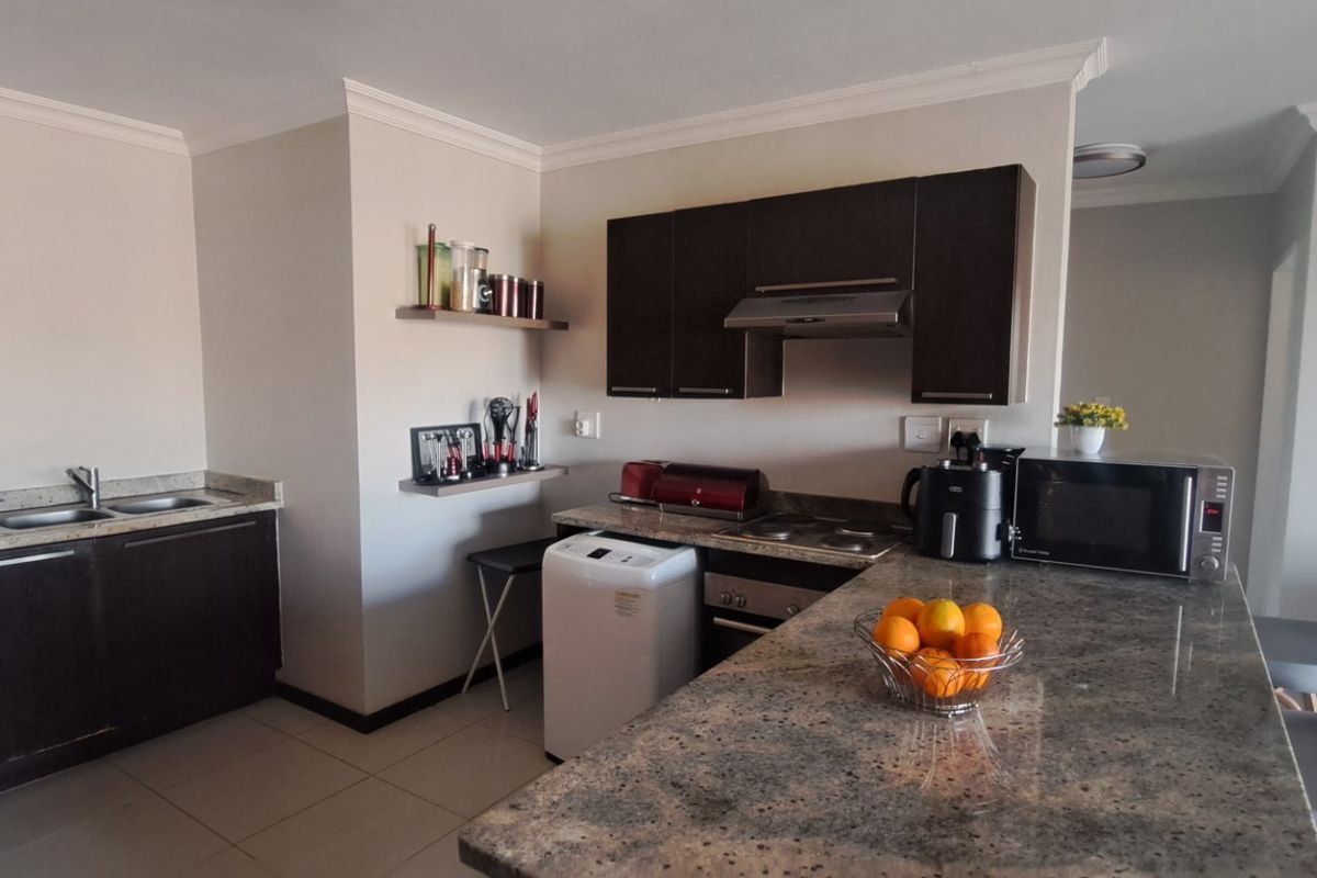 A functional kitchen featuring dark wood cabinetry, granite countertops, a built-in oven, hob, and extractor fan, with tiled flooring throughout.