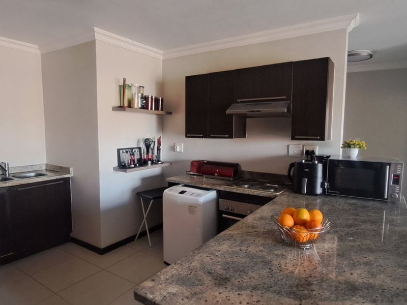 A functional kitchen featuring dark wood cabinetry, granite countertops, a built-in oven, hob, and extractor fan, with tiled flooring throughout.