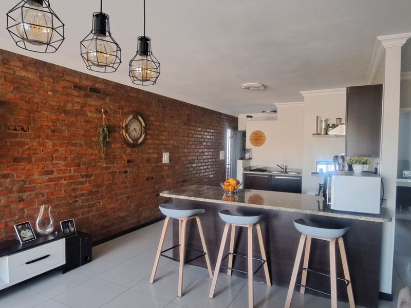 Modern open-plan living area featuring an exposed brick feature wall, granite breakfast bar, and contemporary pendant lighting, seamlessly connecting to the kitchen space.