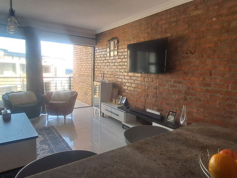 Open-plan living area featuring an exposed brick feature wall, tiled flooring, and large sliding doors leading to an outdoor balcony space.