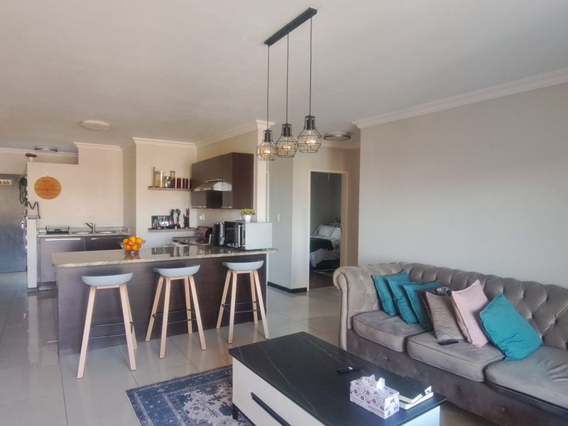 An open-plan living and kitchen area featuring an exposed brick feature wall, tiled flooring, and a breakfast bar with granite countertops.