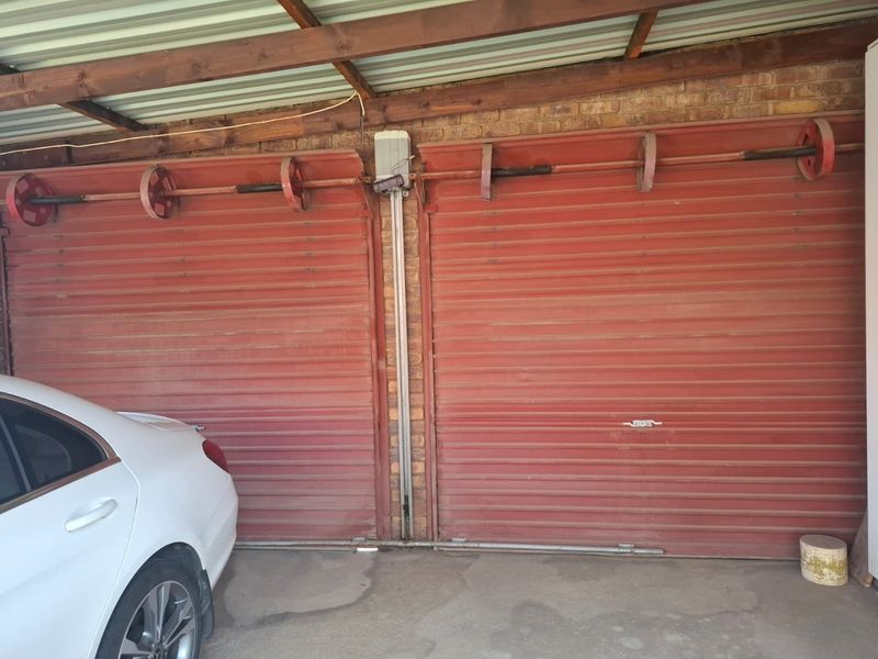 A double garage space featuring red roller shutter doors, exposed timber roof beams, and concrete flooring.