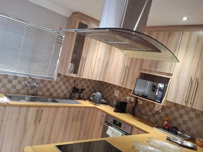 Modern kitchen featuring light wood-finish cabinetry, a central island with an integrated electric hob, stainless steel extractor fan, and a tiled backsplash.