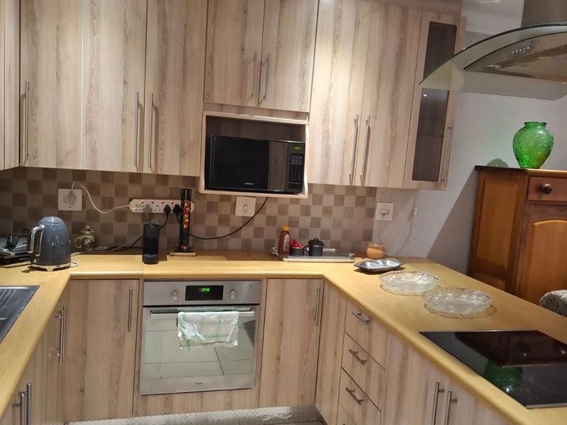 A functional U-shaped kitchen featuring light wood-grain cabinetry, laminate countertops, integrated appliances, and a tiled backsplash with recessed lighting.