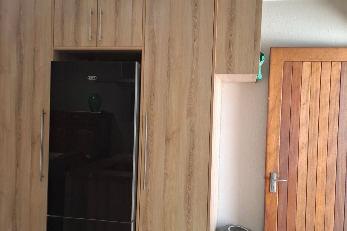 A kitchen area featuring modern timber-look built-in cabinetry and a solid timber door, providing a clean and functional storage solution.