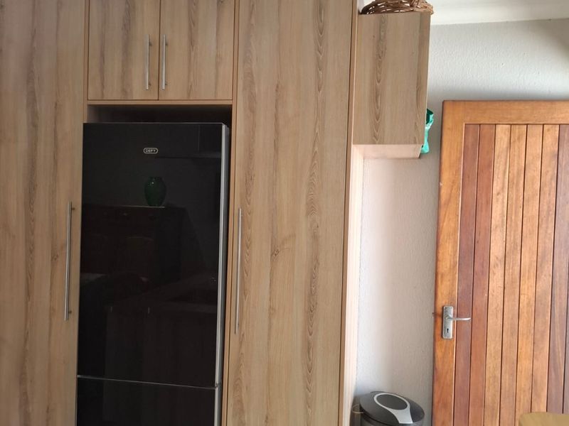 A kitchen area featuring modern timber-look built-in cabinetry and a solid timber door, providing a clean and functional storage solution.
