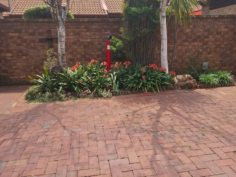 A private rear courtyard featuring red brick paving, a perimeter brick wall, and established garden beds with mature trees.