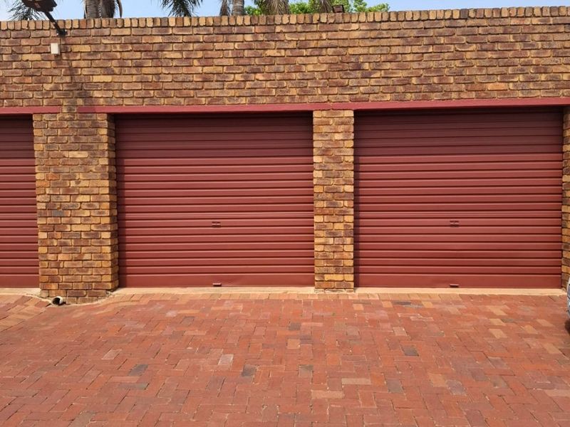A well-maintained exterior view of a multi-car garage featuring brick construction, red roller shutter doors, and a paved driveway.