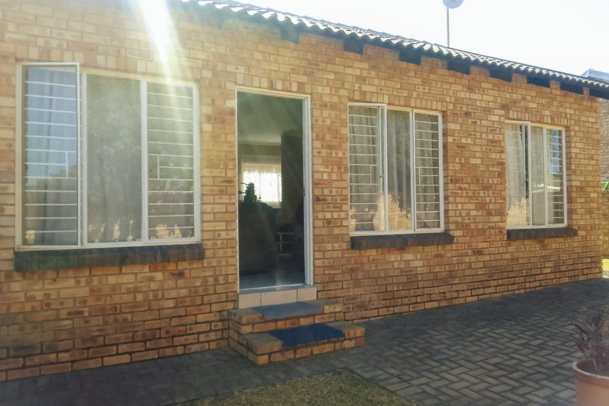 Rear exterior view of a face brick townhouse featuring a paved patio area, security bars on windows, and a tiled roof.