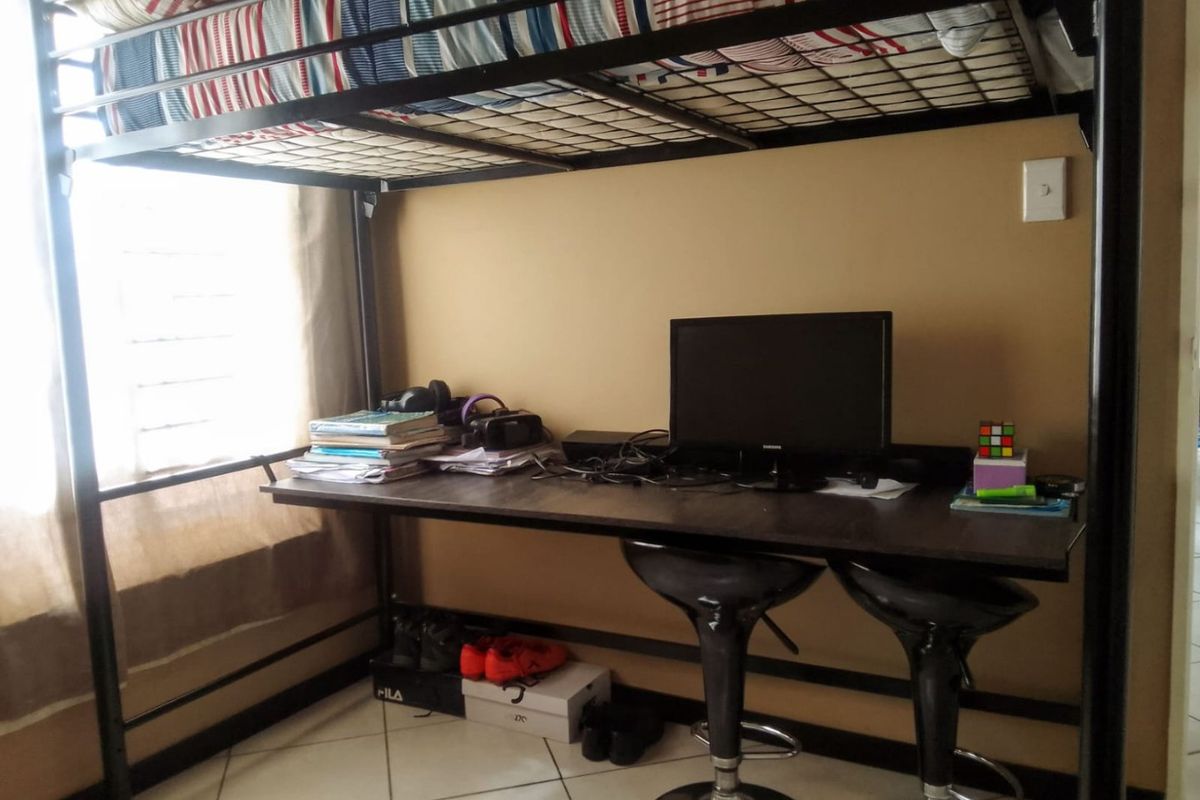 A bedroom featuring tiled flooring and a louvered window, currently utilized with a loft bed and integrated desk workspace.