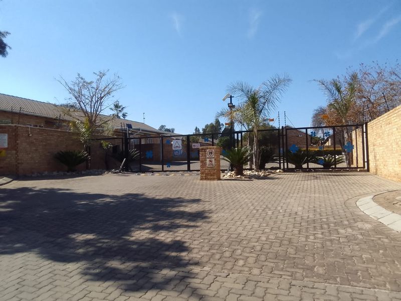 A secure gated entrance to the townhouse complex featuring paved driveway access, brick perimeter walls, and integrated security infrastructure.