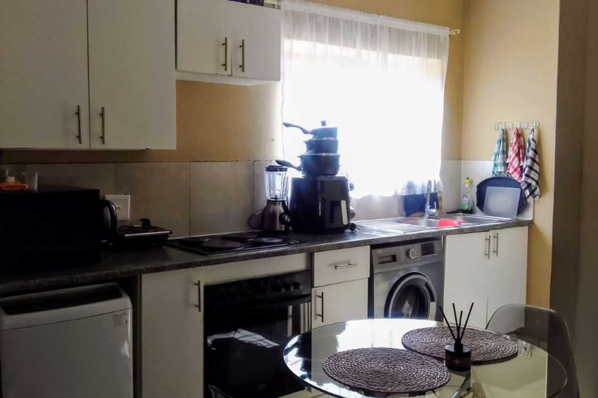 A functional kitchen featuring white cabinetry, laminate countertops, integrated oven and hob, and tiled flooring with a dedicated space for laundry appliances.
