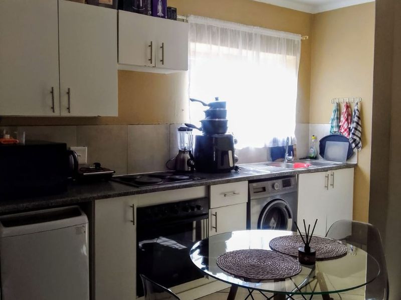 A functional kitchen featuring white cabinetry, laminate countertops, integrated oven and hob, and tiled flooring with a dedicated space for laundry appliances.