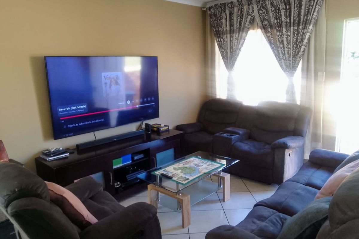 A comfortable living room featuring tiled flooring and large windows with curtain rails, providing a functional space for relaxation.