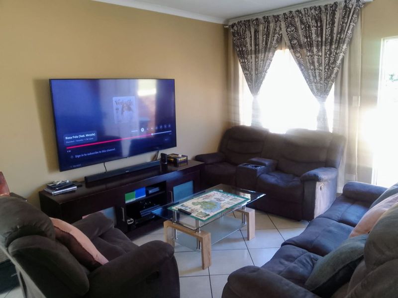 A comfortable living room featuring tiled flooring and large windows with curtain rails, providing a functional space for relaxation.