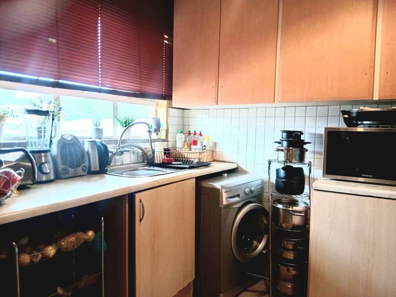 A functional kitchen featuring laminate cabinetry, a tiled backsplash, and a stainless steel sink with integrated space for a washing machine.