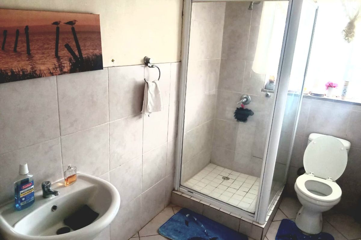 A functional bathroom featuring a pedestal basin, a glass-enclosed shower, and a standard toilet with neutral ceramic tiling throughout.