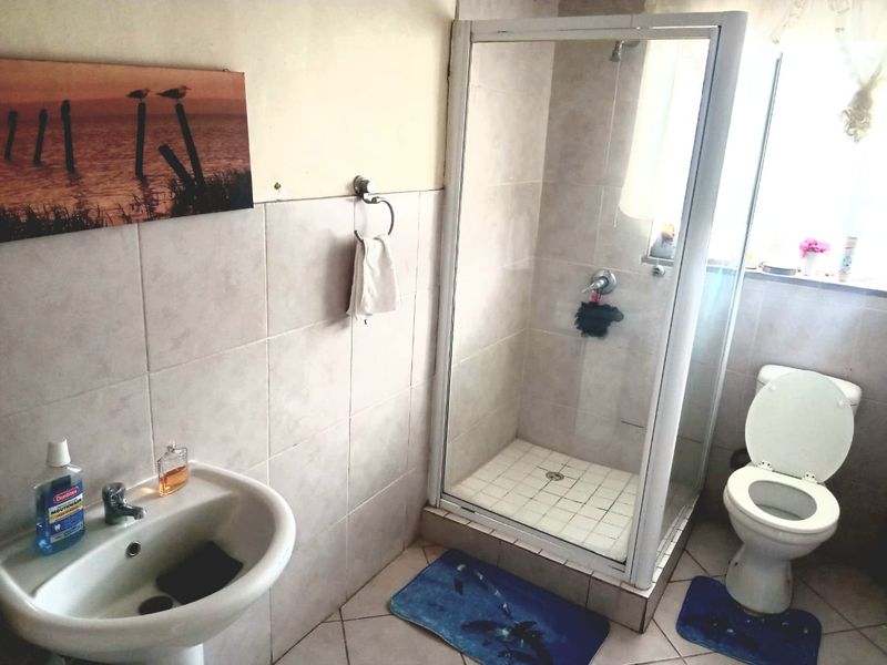 A functional bathroom featuring a pedestal basin, a glass-enclosed shower, and a standard toilet with neutral ceramic tiling throughout.