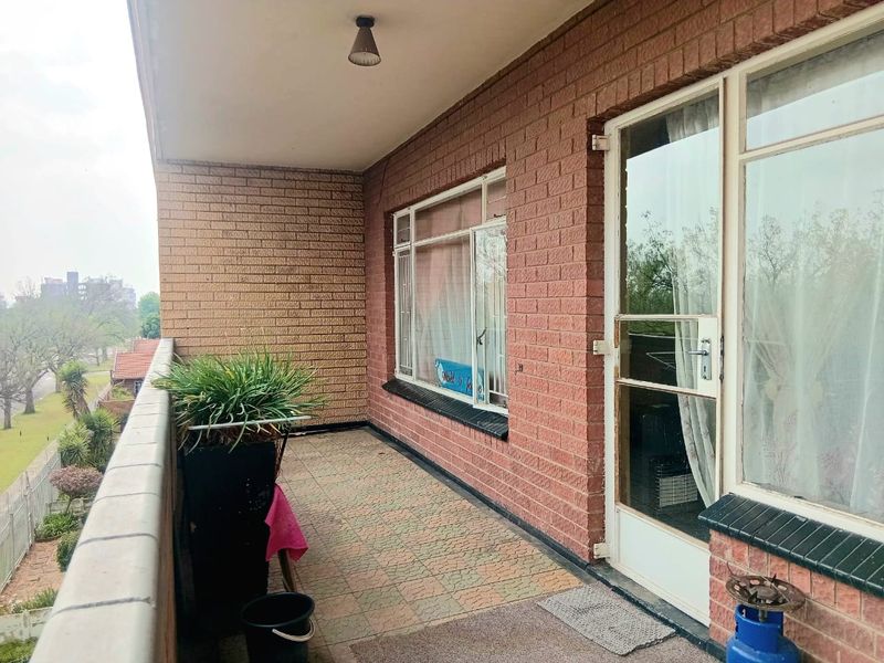 A covered balcony featuring brick walls, tiled flooring, and a metal balustrade, offering an outdoor space with views of the surrounding area.