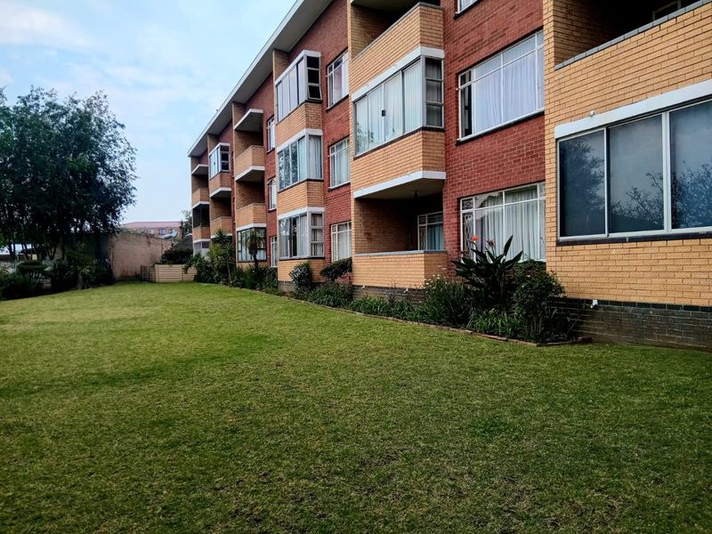 Rear view of a multi-story brick apartment building featuring private balconies and a well-maintained communal lawn area.