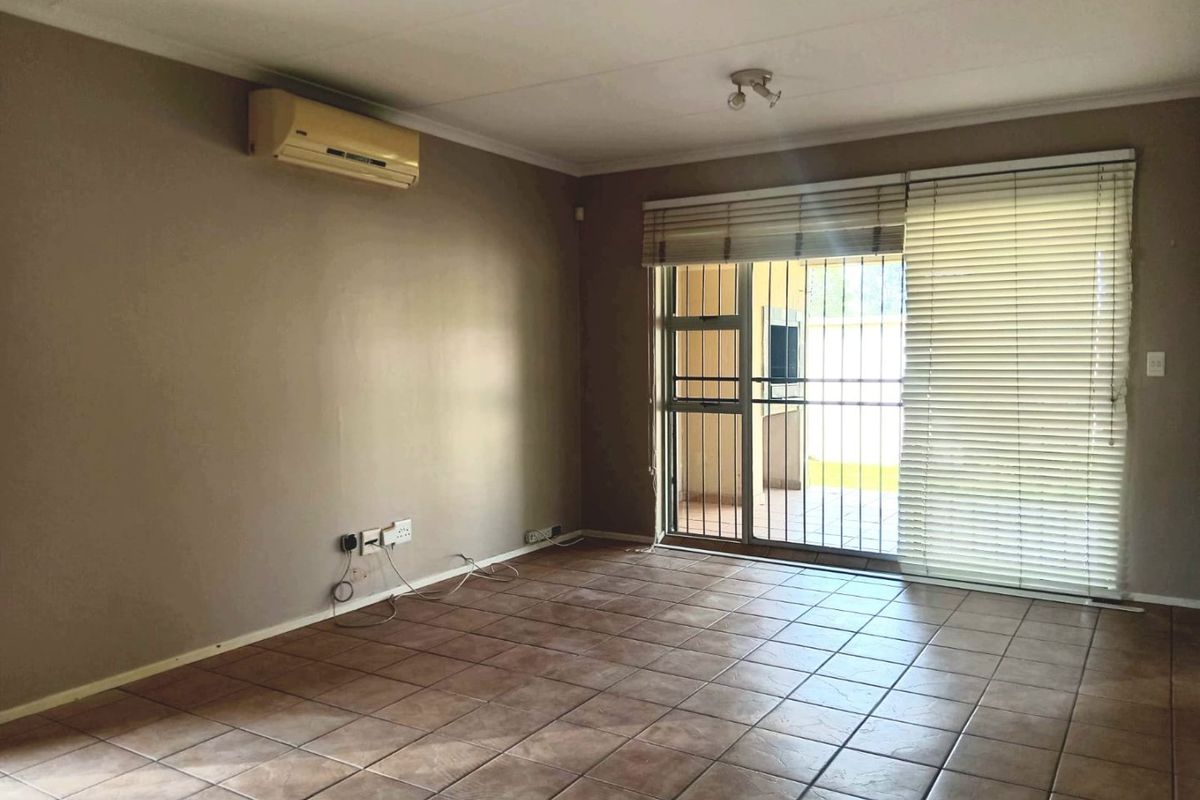 An empty living room featuring tiled flooring, a wall-mounted air conditioning unit, and a sliding glass door with security gate leading to the patio.
