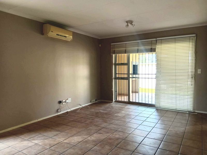 An empty living room featuring tiled flooring, a wall-mounted air conditioning unit, and a sliding glass door with security gate leading to the patio.