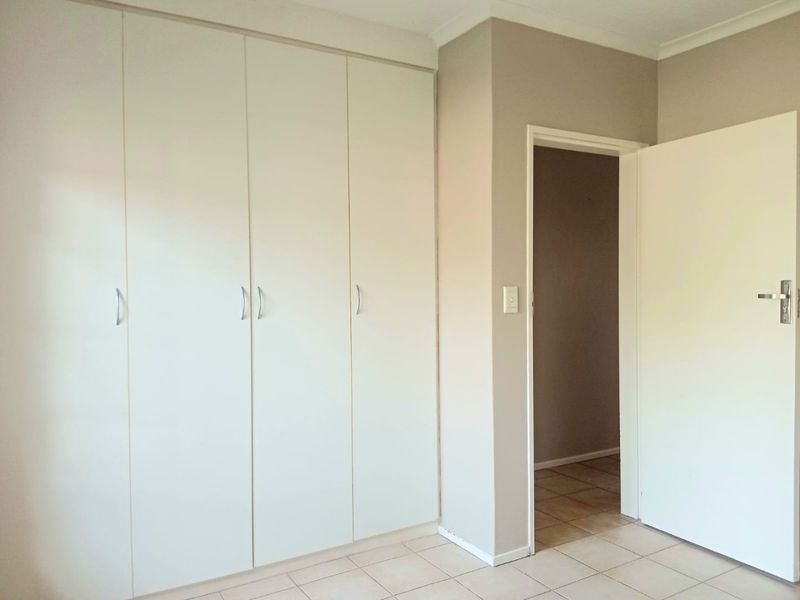 A clean, empty bedroom featuring neutral wall tones, tiled flooring, and ample built-in cupboard storage space.