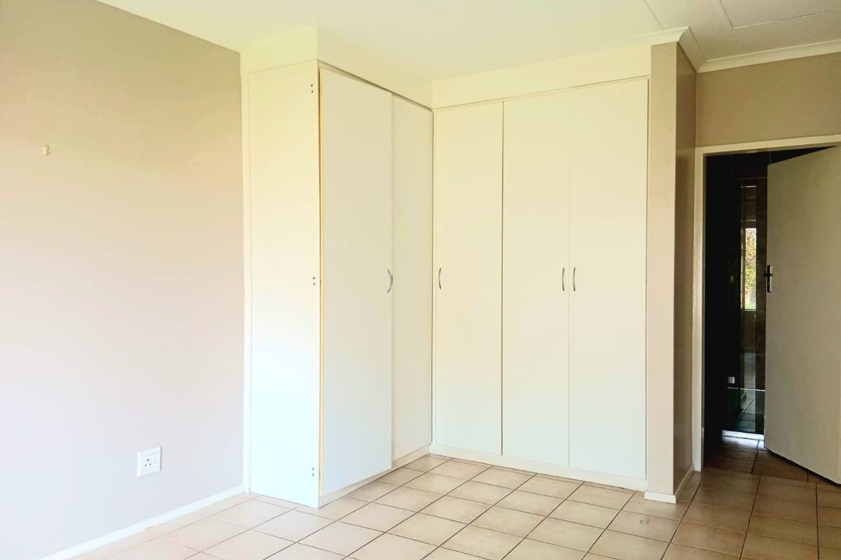 A vacant bedroom featuring neutral wall tones, tiled flooring, and ample built-in cupboard storage space.