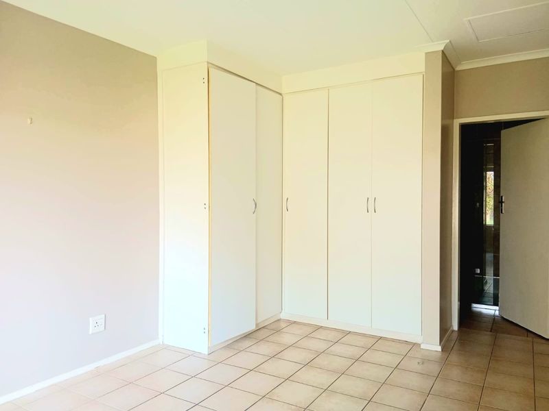 A vacant bedroom featuring neutral wall tones, tiled flooring, and ample built-in cupboard storage space.