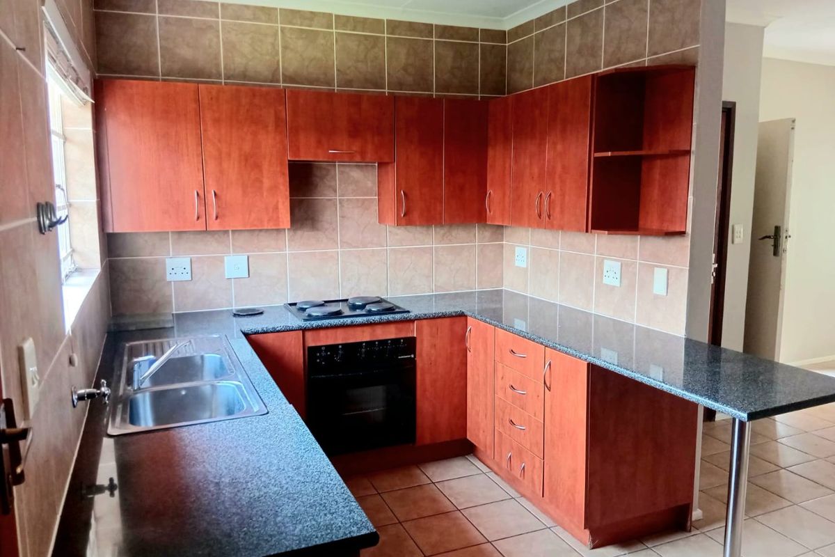 A functional kitchen featuring wooden cabinetry, granite countertops, a built-in oven and hob, and a breakfast nook, finished with tiled flooring and backsplash.