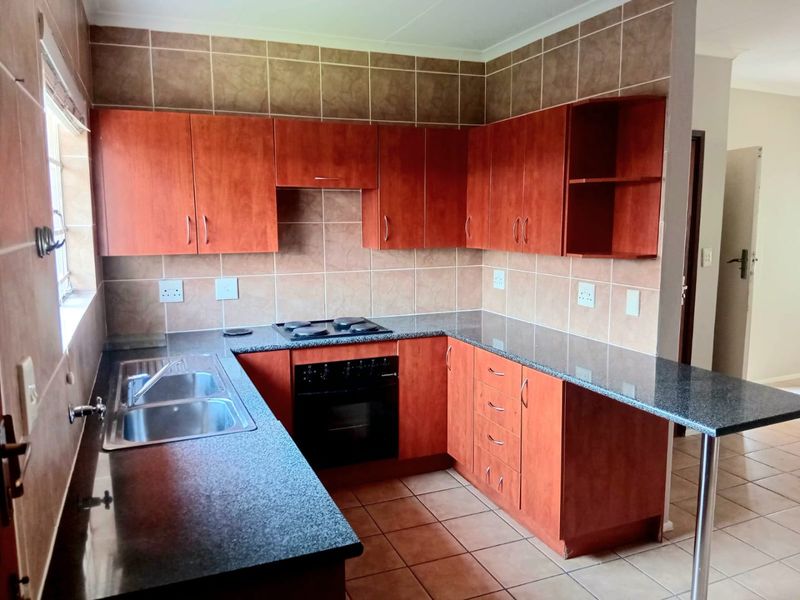 A functional kitchen featuring wooden cabinetry, granite countertops, a built-in oven and hob, and a breakfast nook, finished with tiled flooring and backsplash.